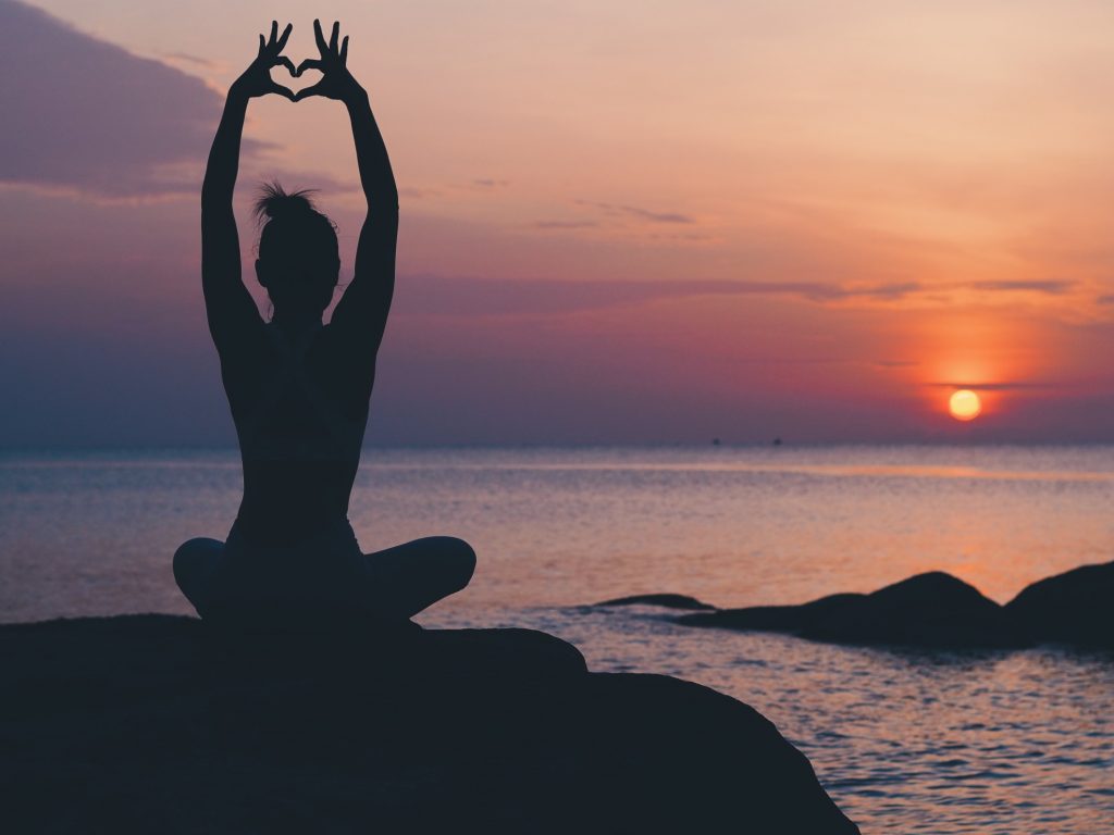 A silhouette of a woman practicing yoga at sunset on a beach